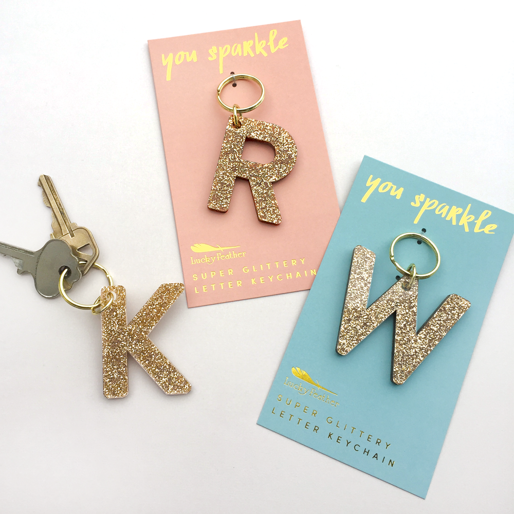 Gold glitter letter keychains 'K' and 'W' on their packaging with 'you sparkle' text.