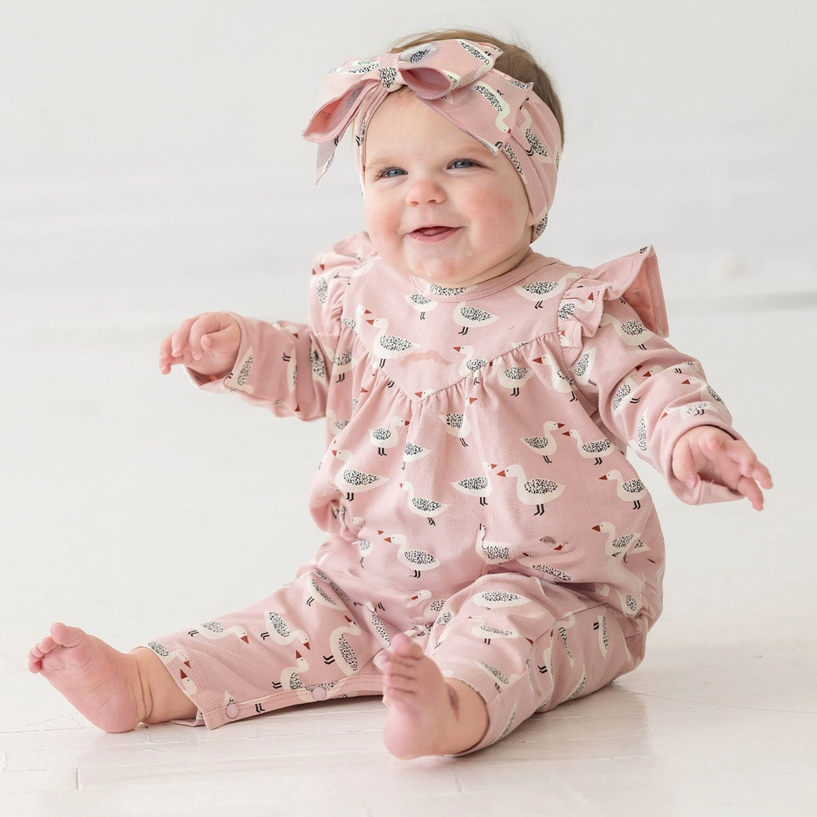 Baby in a pink duck printed outfit with a matching headband on a white background
