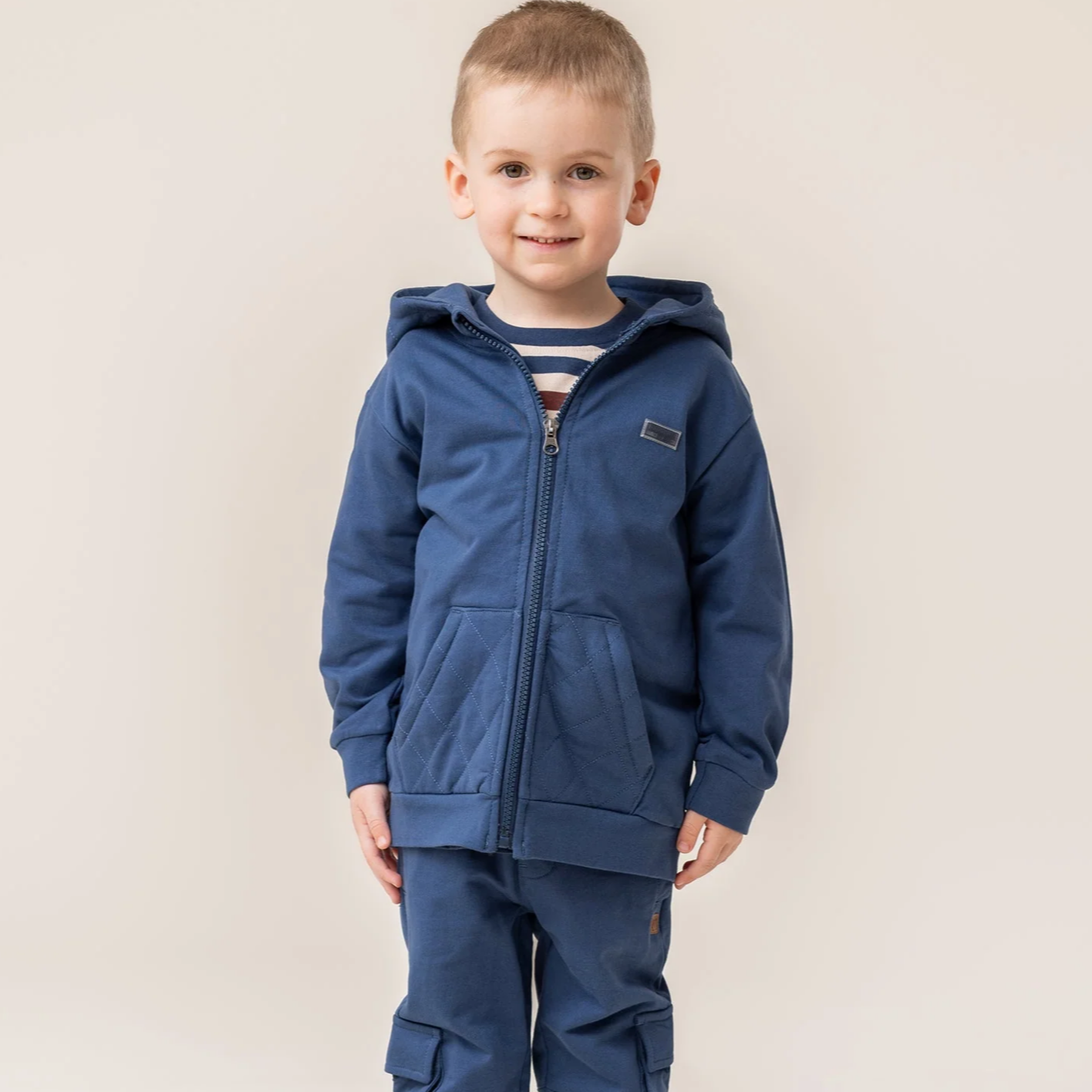 Child wearing a blue tracksuit with a hood on a plain background