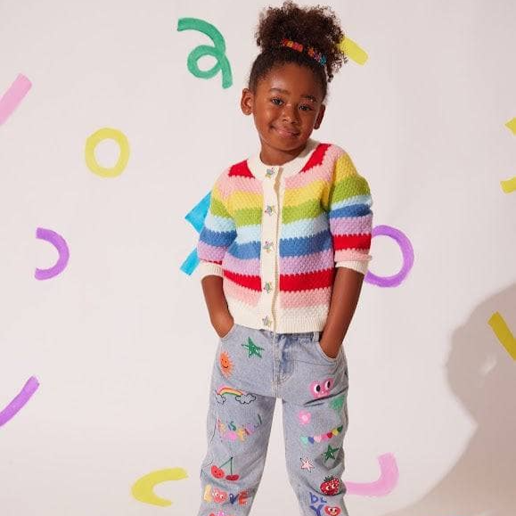 Child wearing a colorful striped sweater and patterned pants against a light background with colorful letters.