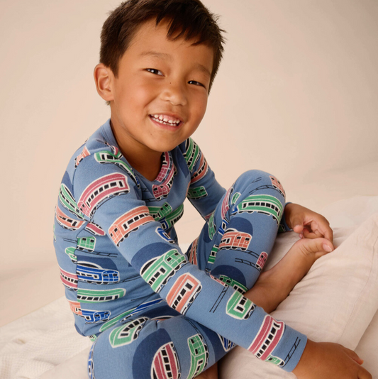 Child wearing blue pajamas with train pattern sitting on a white surface