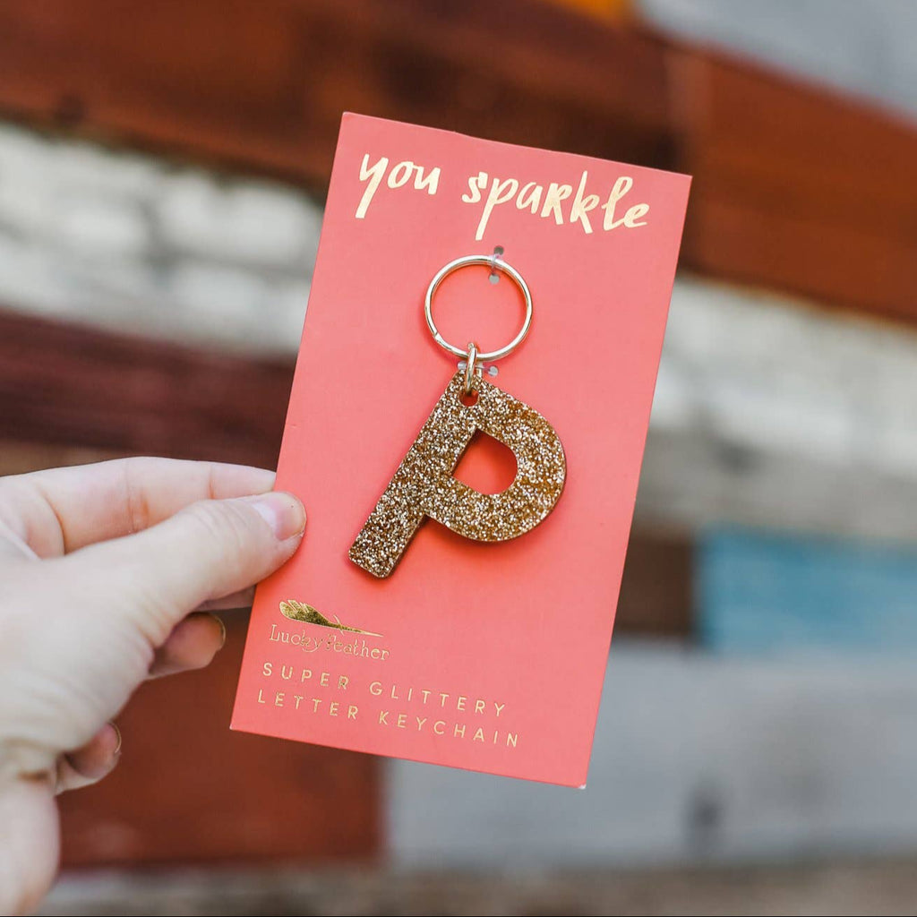Gold letter 'P' keychain on a pink card with 'you sparkle' text, held by a hand.