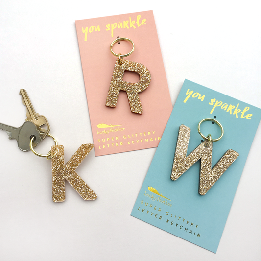 Gold glitter letter keychains 'K' and 'W' on their packaging with 'you sparkle' text.