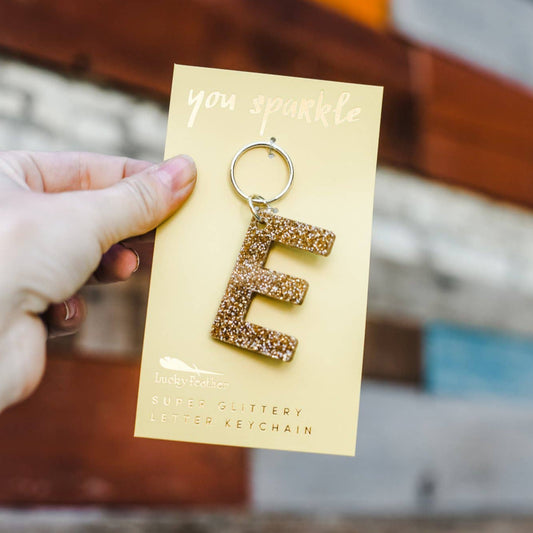 Gold letter 'E' keychain on a yellow card held by a hand with a blurred background