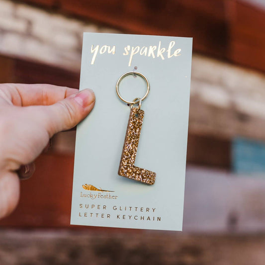 Hand holding a keychain with 'L' design on a card that says 'you sparkle'.