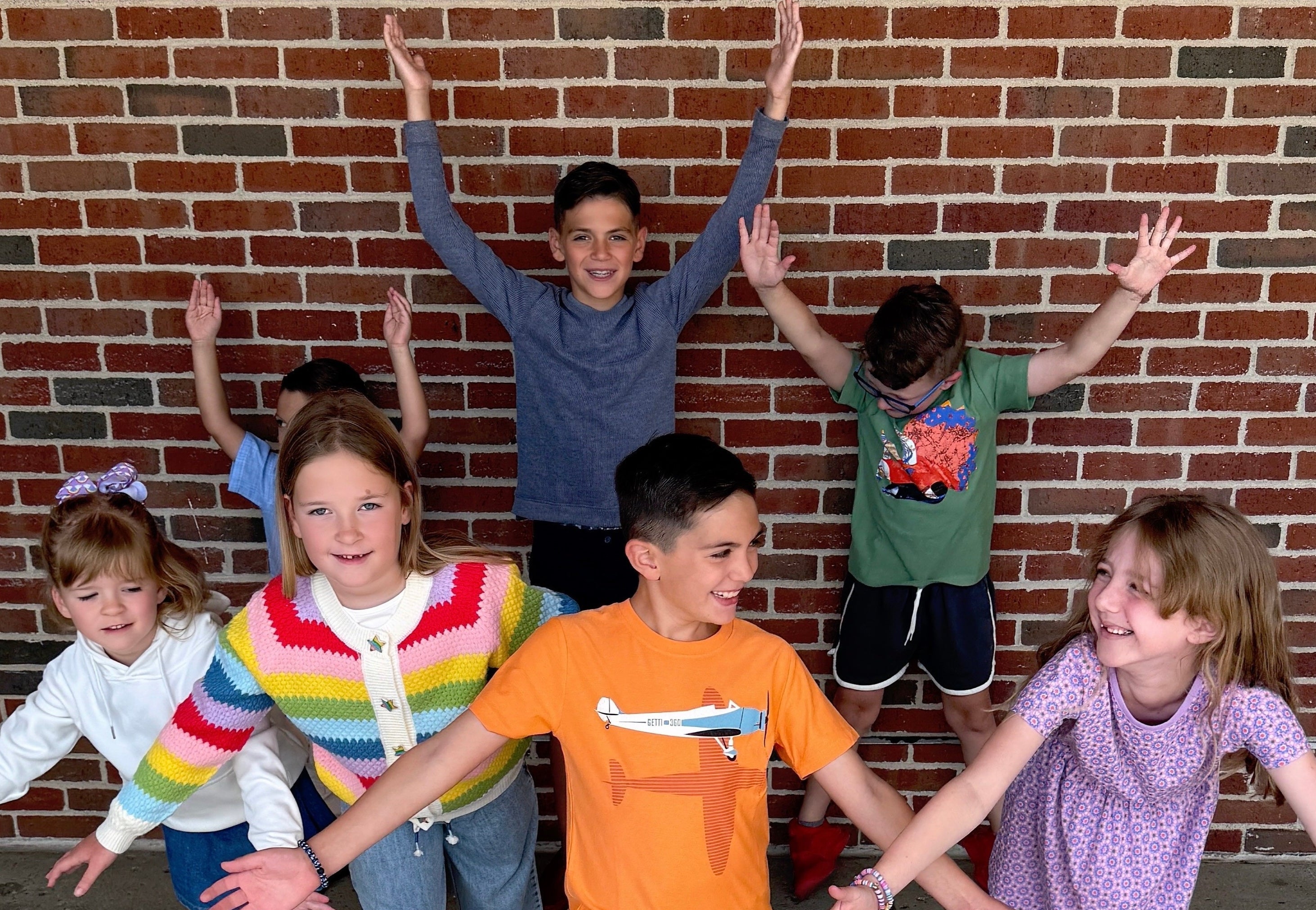 Children posing with arms raised against a brick wall