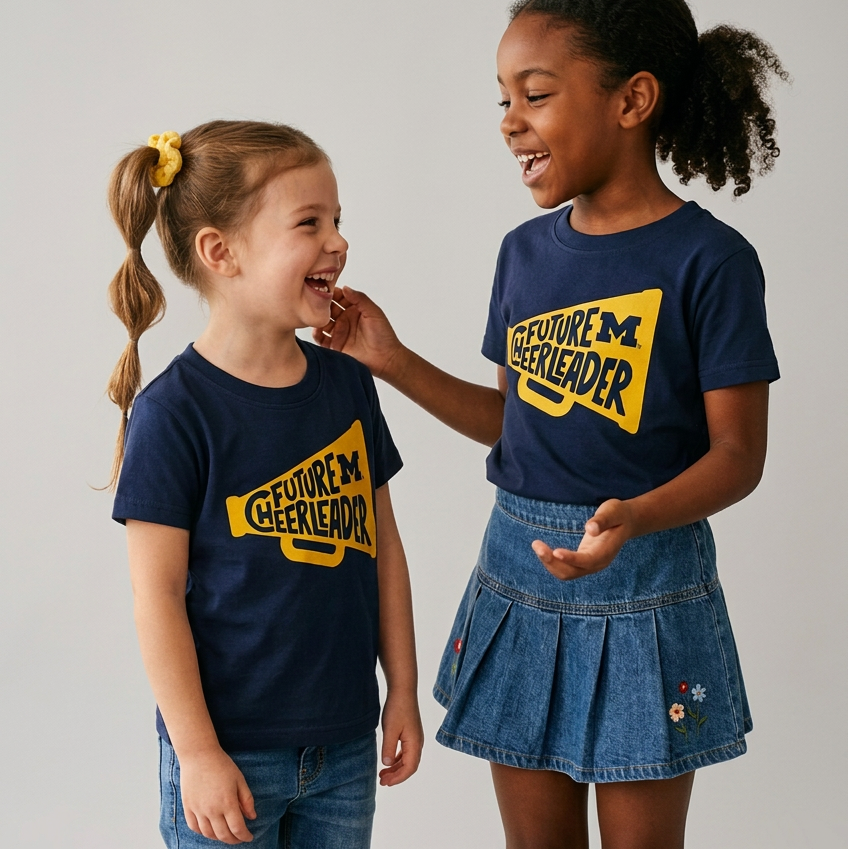 A navy blue short-sleeve t-shirt for toddlers, featuring a yellow megaphone graphic on the chest with the text 'FUTURE M CHEERLEADER' in navy blue.