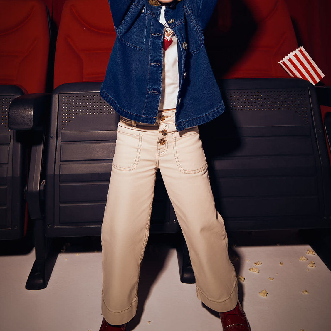 Child in a movie theater holding popcorn, with red seats and dim lighting.